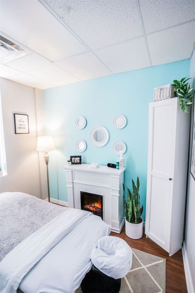 Treatment room with a massage table, soft blanket, electric fireplace and plants