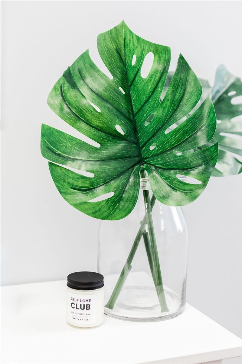 Monstera leaves in a glass vase beside a small candle